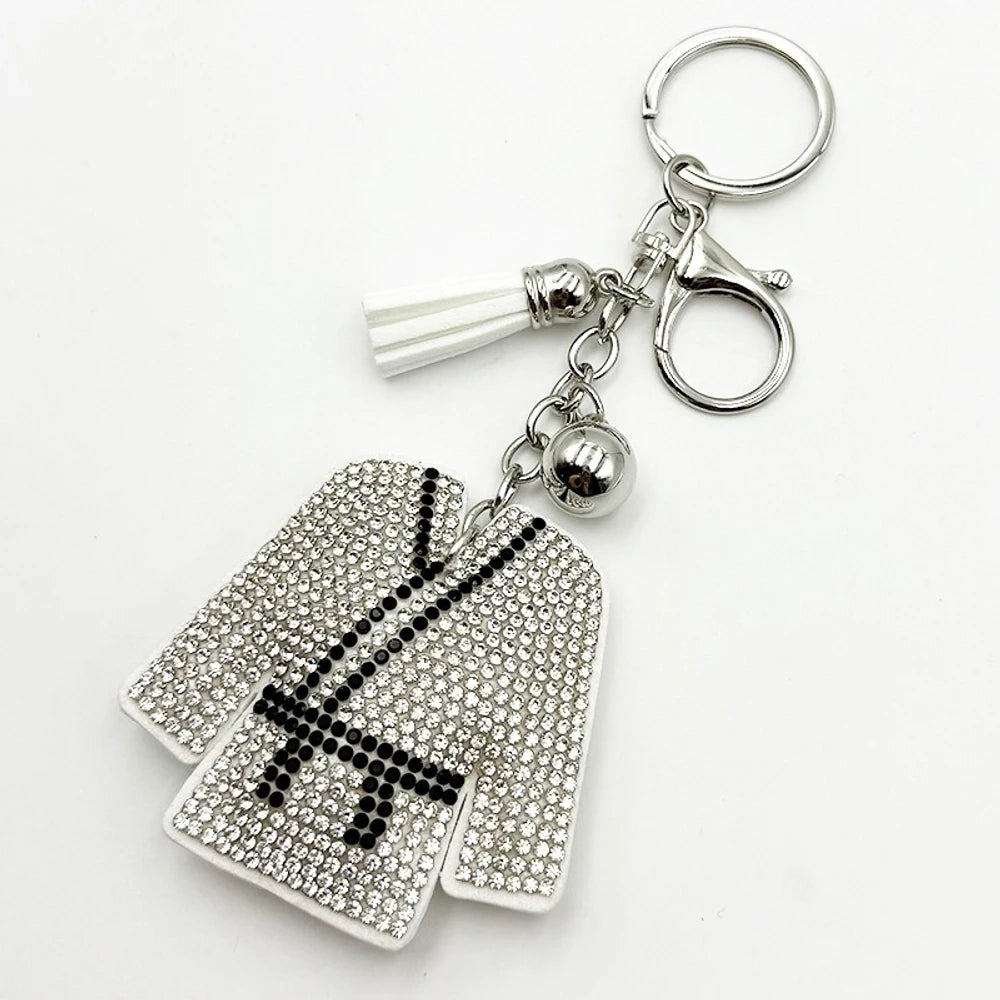 Silver rhinestone-encrusted baseball jacket keychain charm with black NY logo, white tassel, silver bell, and lobster clasp on white background.