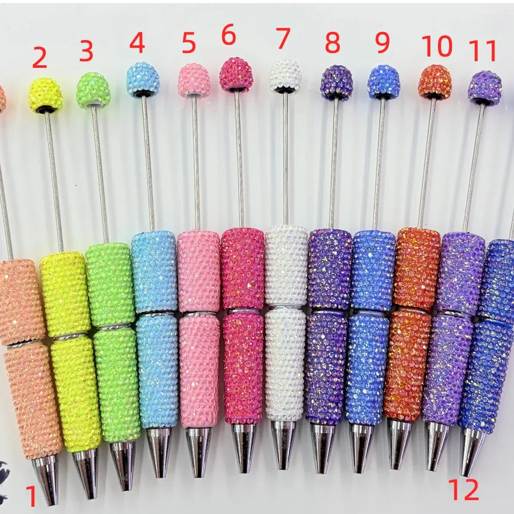 12 rhinestone beadable pens in assorted sparkle crystal colors including yellow, green, blue, pink, hot pink, white, purple, orange, and lavender with silver metal tips and rhinestone-studded barrel and top bead, numbered 1 through 12.