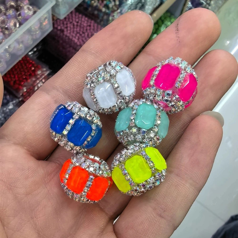 Six colorful rhinestone-bordered resin square fancy beads in white, hot pink, blue, teal, orange, and neon yellow held in a hand, perfect for beadable pens, keychains, and DIY jewelry making.