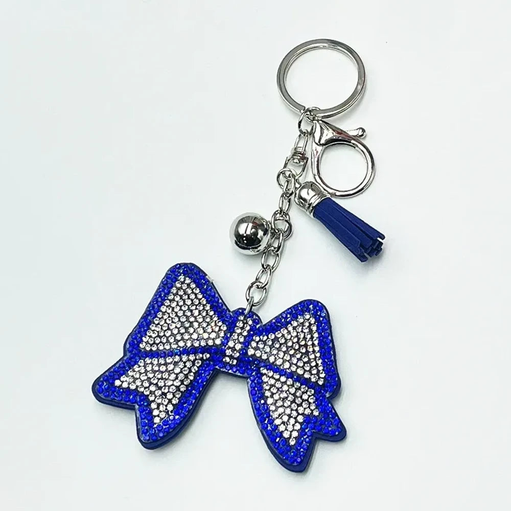 Two rhinestone-encrusted bow keychains with leather tassels and silver bell pendants in pink and brown colorways on a white background. - Blue