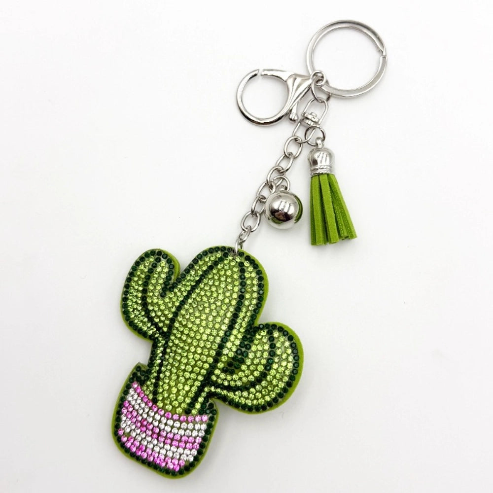 Rhinestone cactus keychain charm decorated with green and pink crystal beads, silver lobster clasp, bell, and green suede tassel on white background.
