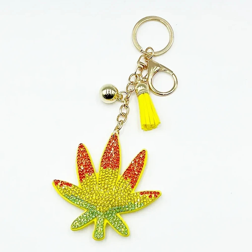 Rhinestone cannabis marijuana leaf keychain charm with yellow tassel and gold chain, decorated with green, yellow, and red crystal rhinestones on a cream leather bag. - Orange