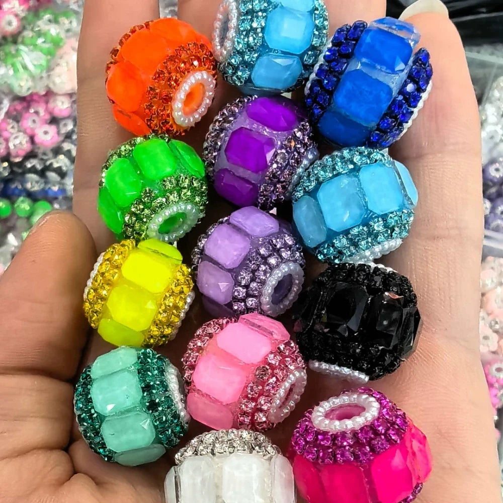 Assorted colorful rhinestone-encrusted chunky round fancy beads in orange, green, yellow, teal, purple, lavender, blue, black, pink, white and hot pink held in a hand, showing pearl and crystal accents around each bead.