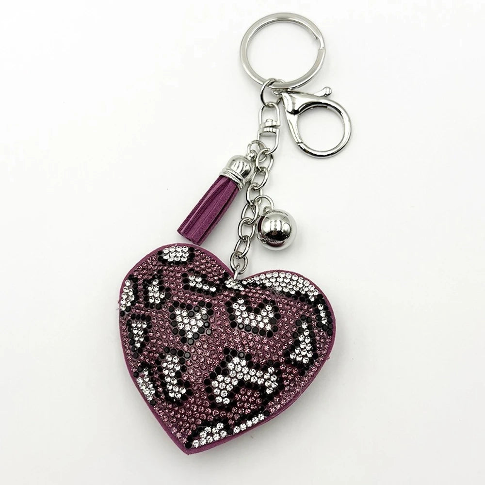 Four rhinestone crystal leopard print heart-shaped keychain charms in pink, purple, brown, and black with silver tassel and bell accents on white background. - Coffee