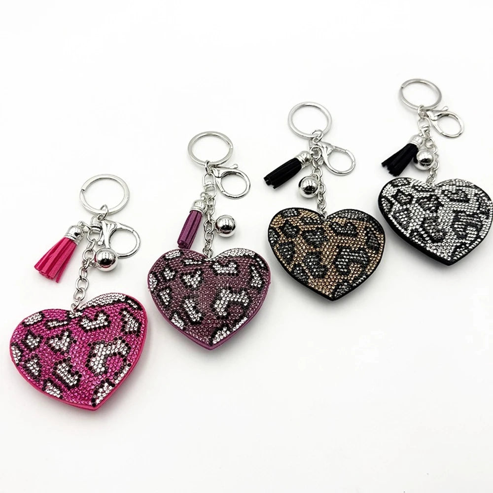 Four rhinestone crystal leopard print heart-shaped keychain charms in pink, purple, brown, and black with silver tassel and bell accents on white background. - Random Mixed