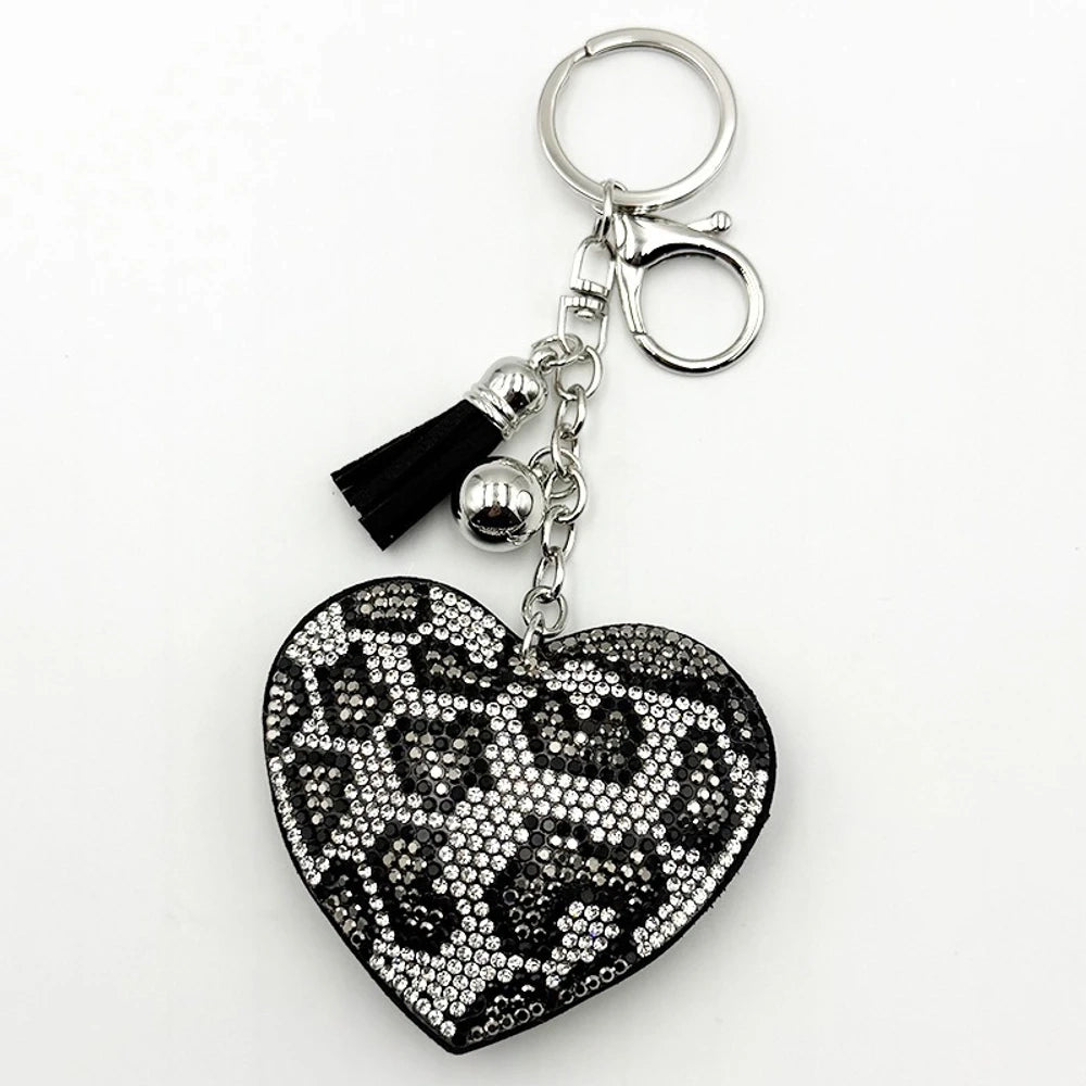 Four rhinestone crystal leopard print heart-shaped keychain charms in pink, purple, brown, and black with silver tassel and bell accents on white background. - Silver