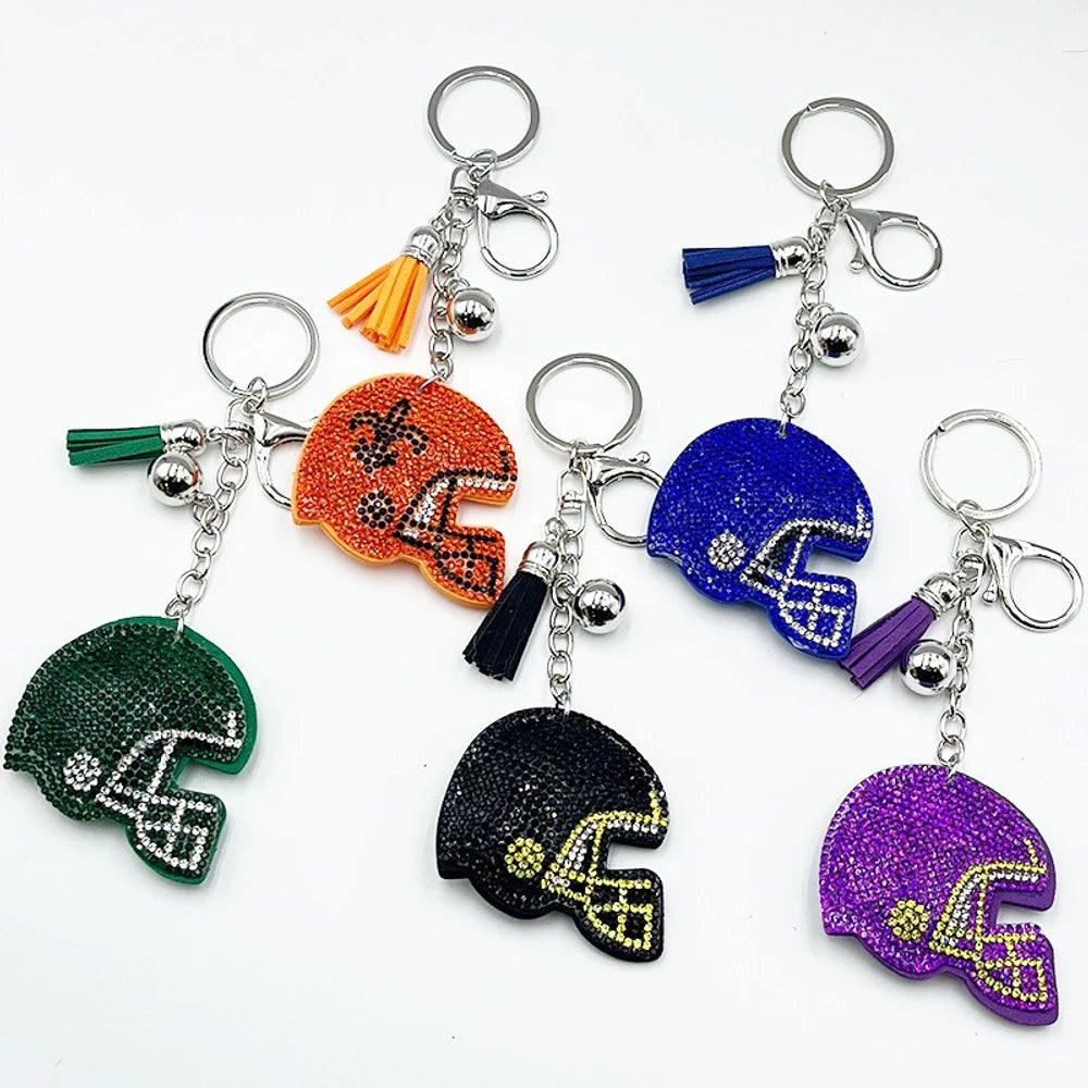 Five rhinestone-covered football helmet keychain charms in green, orange, black, blue, and purple with tassel and bell accents on silver key rings