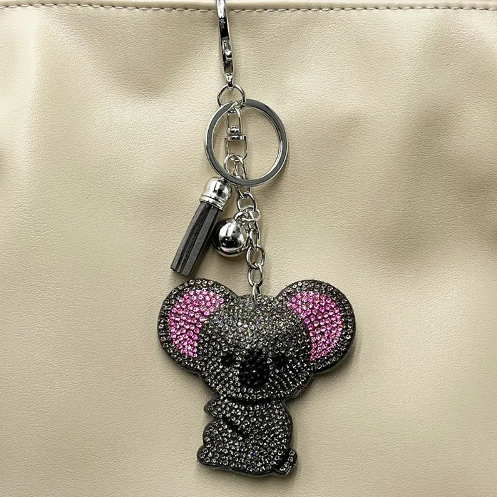 Rhinestone koala bear keychain charm covered in gray and pink crystals with silver chain and tassel, displayed on cream leather bag