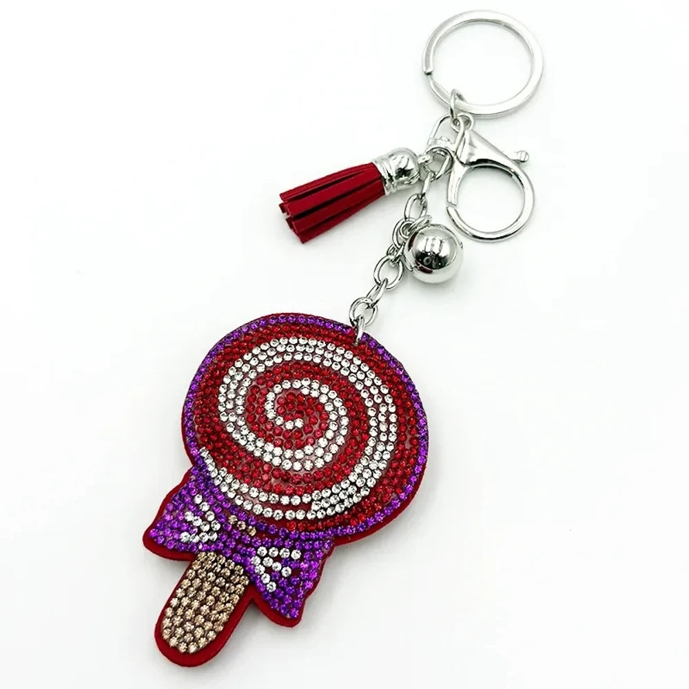 Two rhinestone-studded lollipop charm keychains in teal/blue and red/purple with tassels, silver rings, and bell accents for DIY jewelry making and keychains. - Red