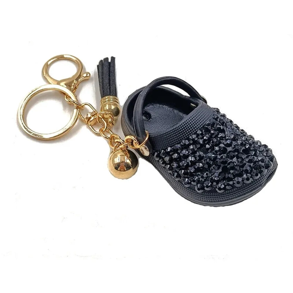 Eight colorful rhinestone-encrusted mini croc shoe keychain charms with gold chain and tassel in yellow, green, blue, pink, lavender, red, white, black, and purple arranged in a circle on a white surface. - Black