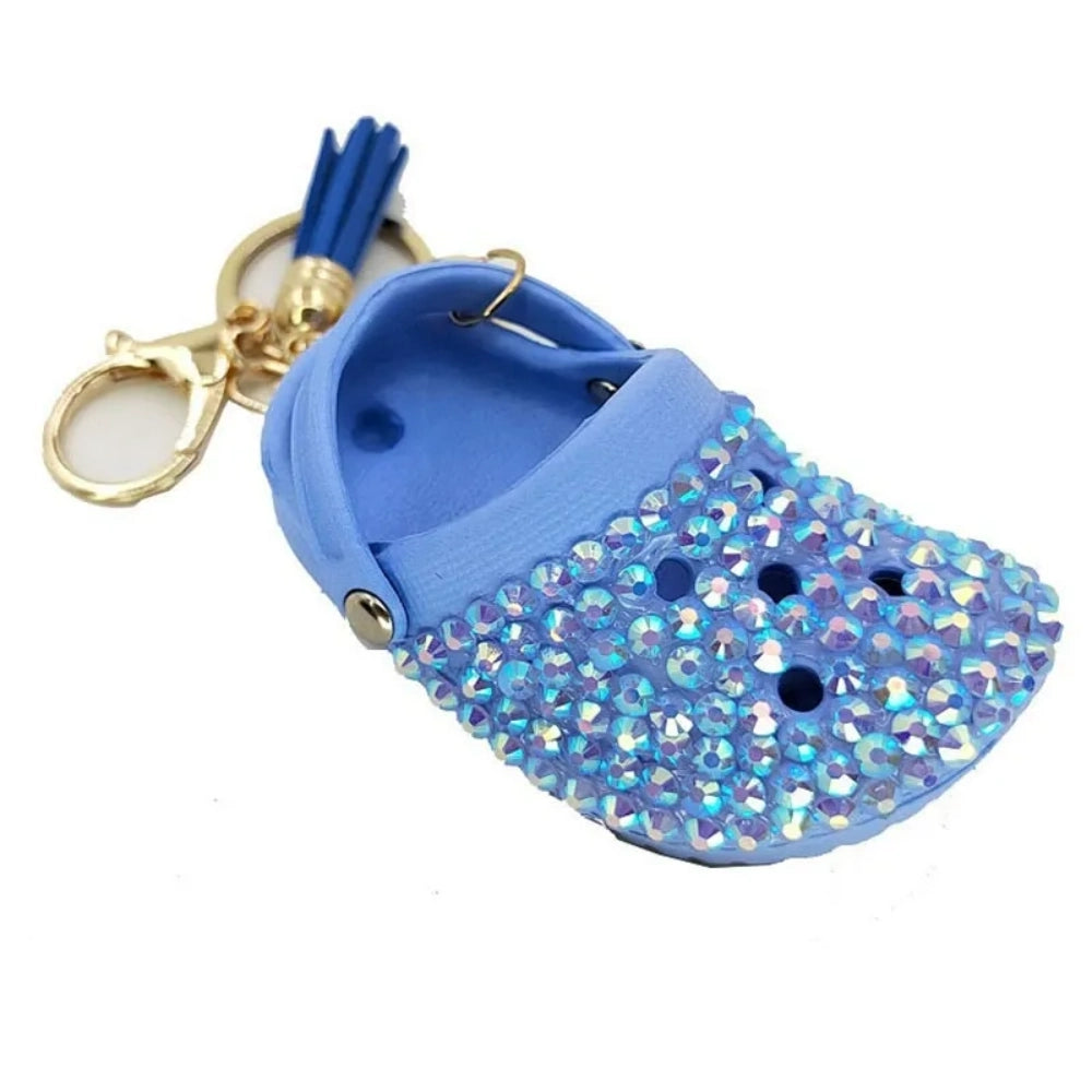 Eight colorful rhinestone-encrusted mini croc shoe keychain charms with gold chain and tassel in yellow, green, blue, pink, lavender, red, white, black, and purple arranged in a circle on a white surface. - Blue