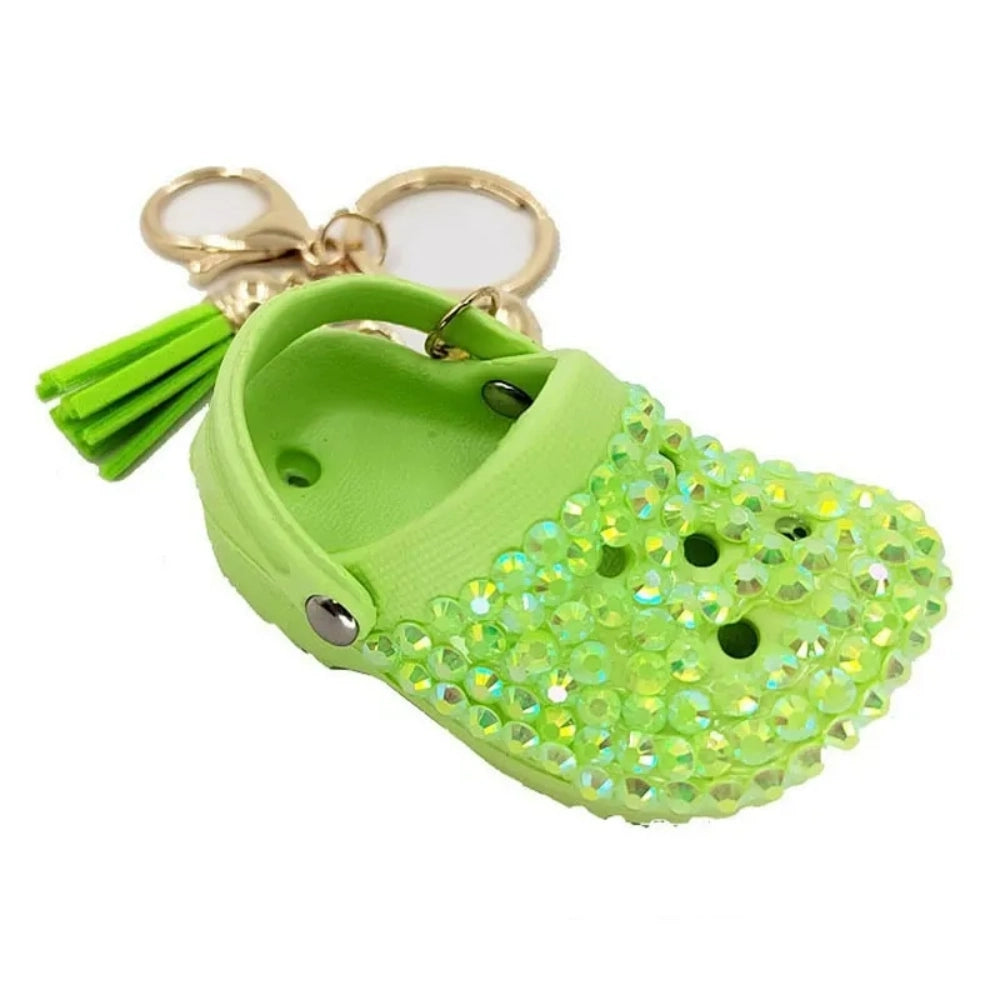 Eight colorful rhinestone-encrusted mini croc shoe keychain charms with gold chain and tassel in yellow, green, blue, pink, lavender, red, white, black, and purple arranged in a circle on a white surface. - Green