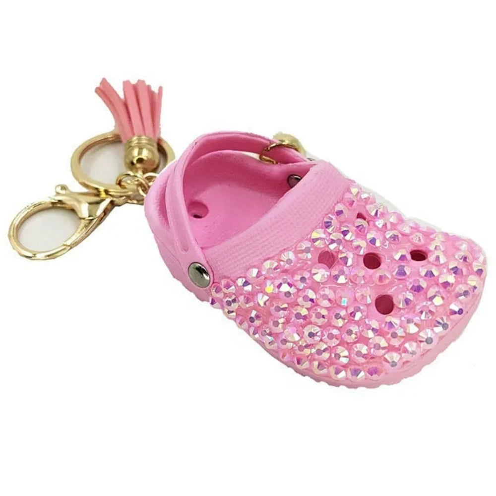 Eight colorful rhinestone-encrusted mini croc shoe keychain charms with gold chain and tassel in yellow, green, blue, pink, lavender, red, white, black, and purple arranged in a circle on a white surface. - Pink