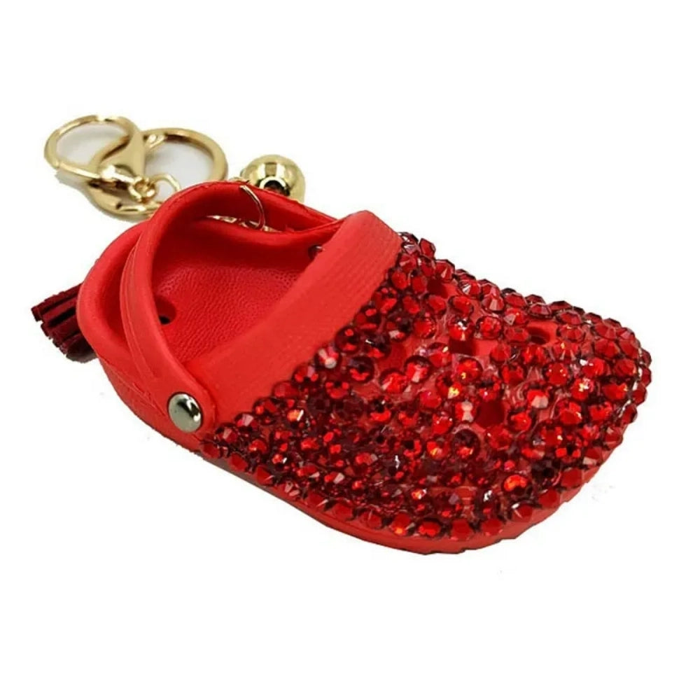 Eight colorful rhinestone-encrusted mini croc shoe keychain charms with gold chain and tassel in yellow, green, blue, pink, lavender, red, white, black, and purple arranged in a circle on a white surface. - Red
