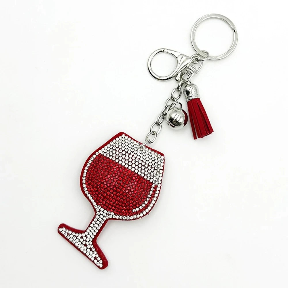 Four rhinestone-covered wine glass keychain charms in red, pink, blue, and black with matching tassels and silver bell accents on white background. - Red