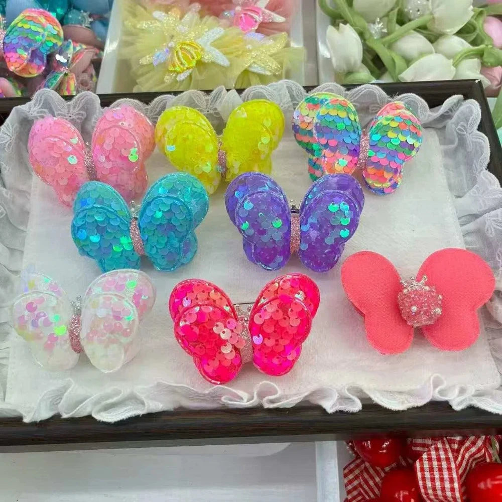 Assorted colorful sequin butterfly hair clip embellishments in pink, yellow, teal, purple, white, hot pink, and coral on a white lace display tray, ideal for DIY crafts and jewelry making.