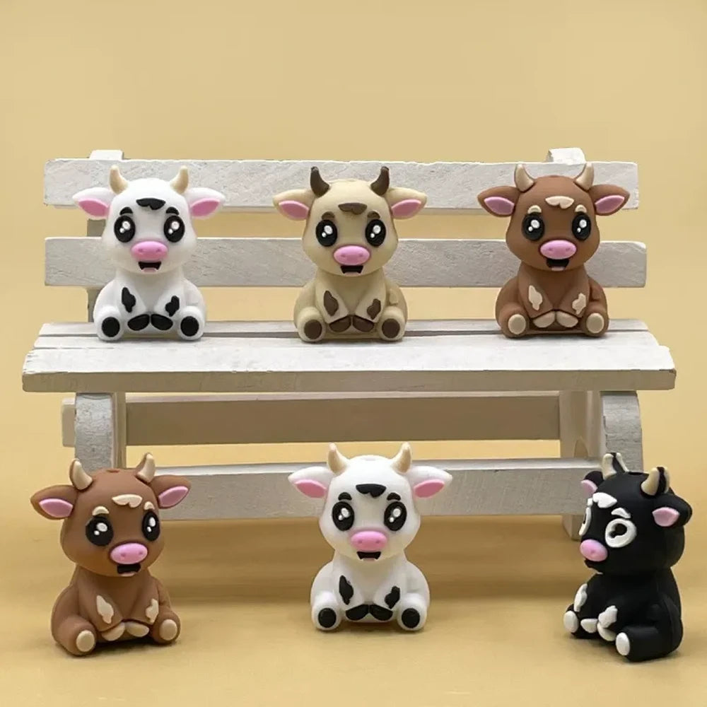 Set of 6 cute 3D baby cow silicone focal beads in white, tan, brown, and black color variants displayed on a miniature wooden bench against a yellow background.