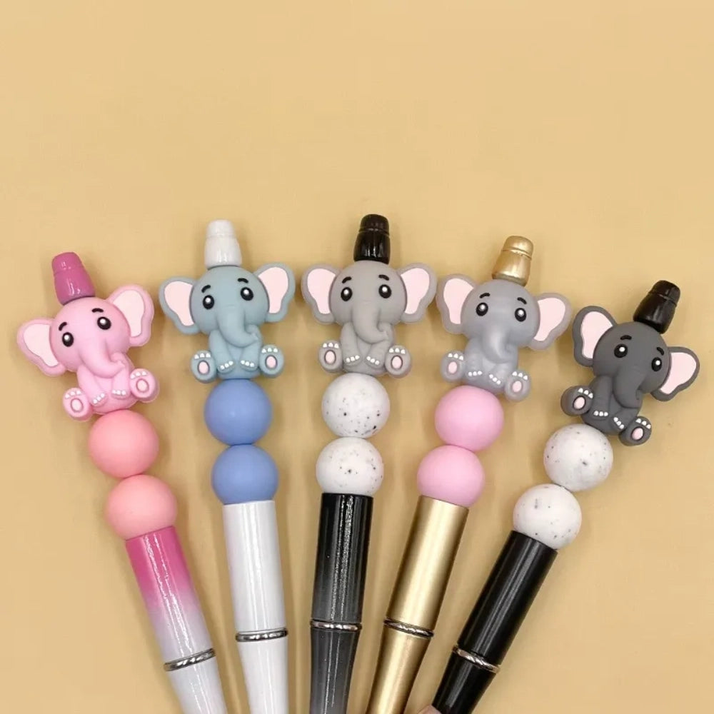 Five cute 3D baby elephant silicone focal beads in light gray, medium gray, dark gray, blue, and pink colors, sitting posed with pink inner ears and toenails, displayed on a white platform against a warm beige background. - Random Mixed