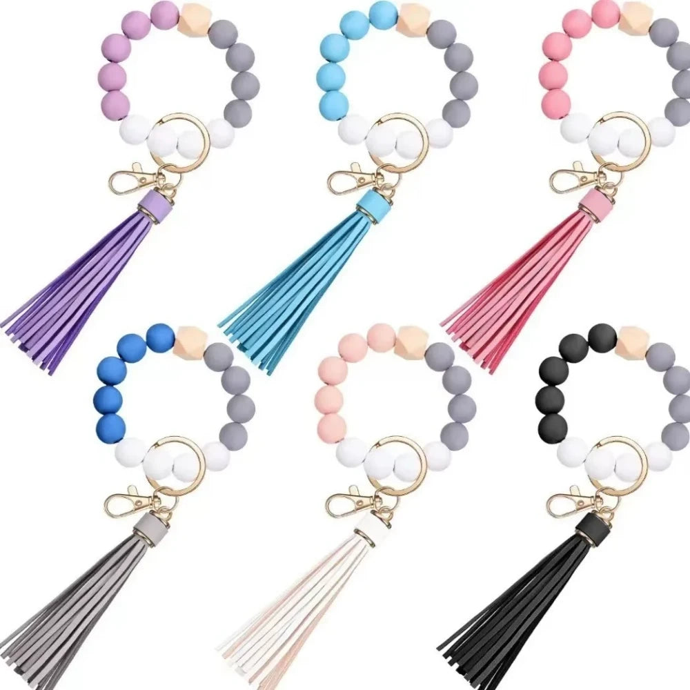 Set of 6 silicone bead wristlet keychains with colorful leather tassels in purple, blue, pink, gray, blush, and black on gold swivel clasps for DIY jewelry making.