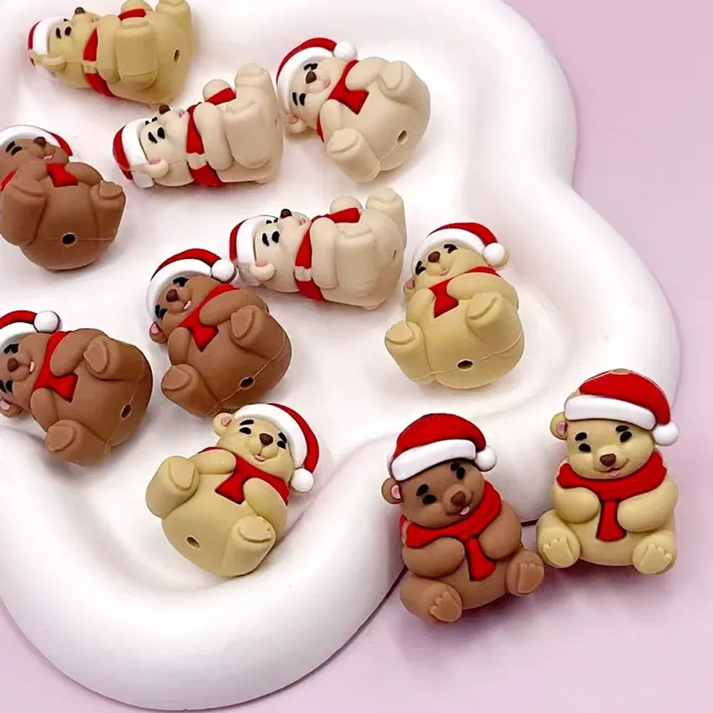 3D Christmas Santa Bear silicone focal beads in tan and brown colors wearing red Santa hats and scarves, displayed on white clay surface with pink background