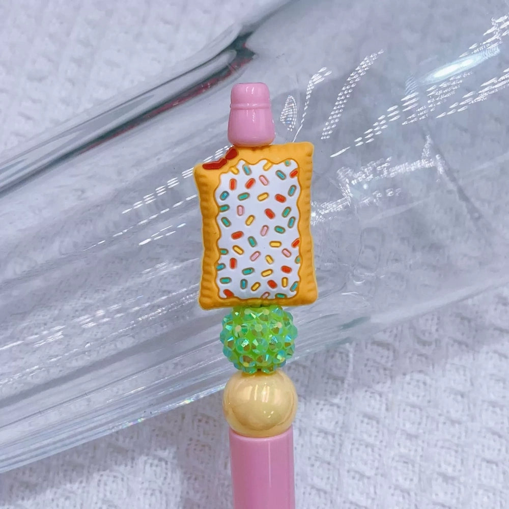 Miniature 3D Pop Tart silicone focal beads with pink and white frosting and colorful sprinkles, shown on green and pink beadable pens alongside loose focal beads on a white waffle texture background. - 1