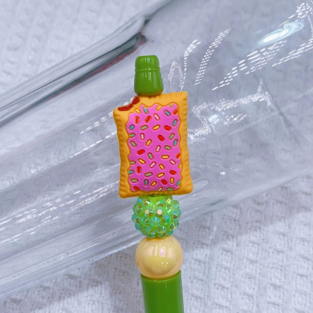 Miniature 3D Pop Tart silicone focal beads with pink and white frosting and colorful sprinkles, shown on green and pink beadable pens alongside loose focal beads on a white waffle texture background. - 2