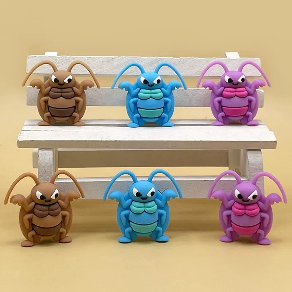 Six cartoon angry cockroach silicone focal beads in brown, blue, and purple displayed on a miniature white wooden bench against a yellow background.