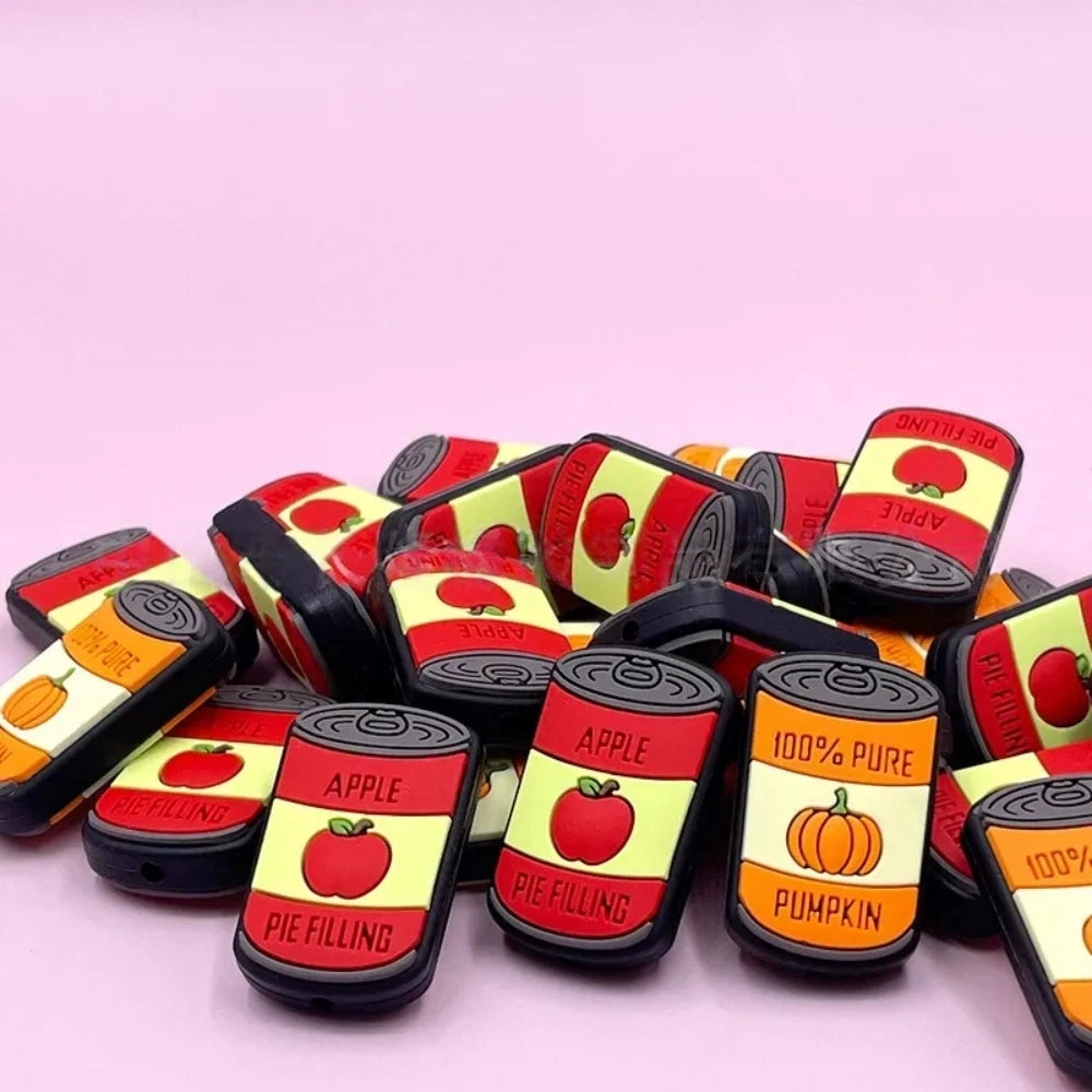 Silicone focal beads shaped like mini canned goods with Apple Pie Filling and 100% Pure Pumpkin labels, displayed in a pile on a pink background. - Random Mixed