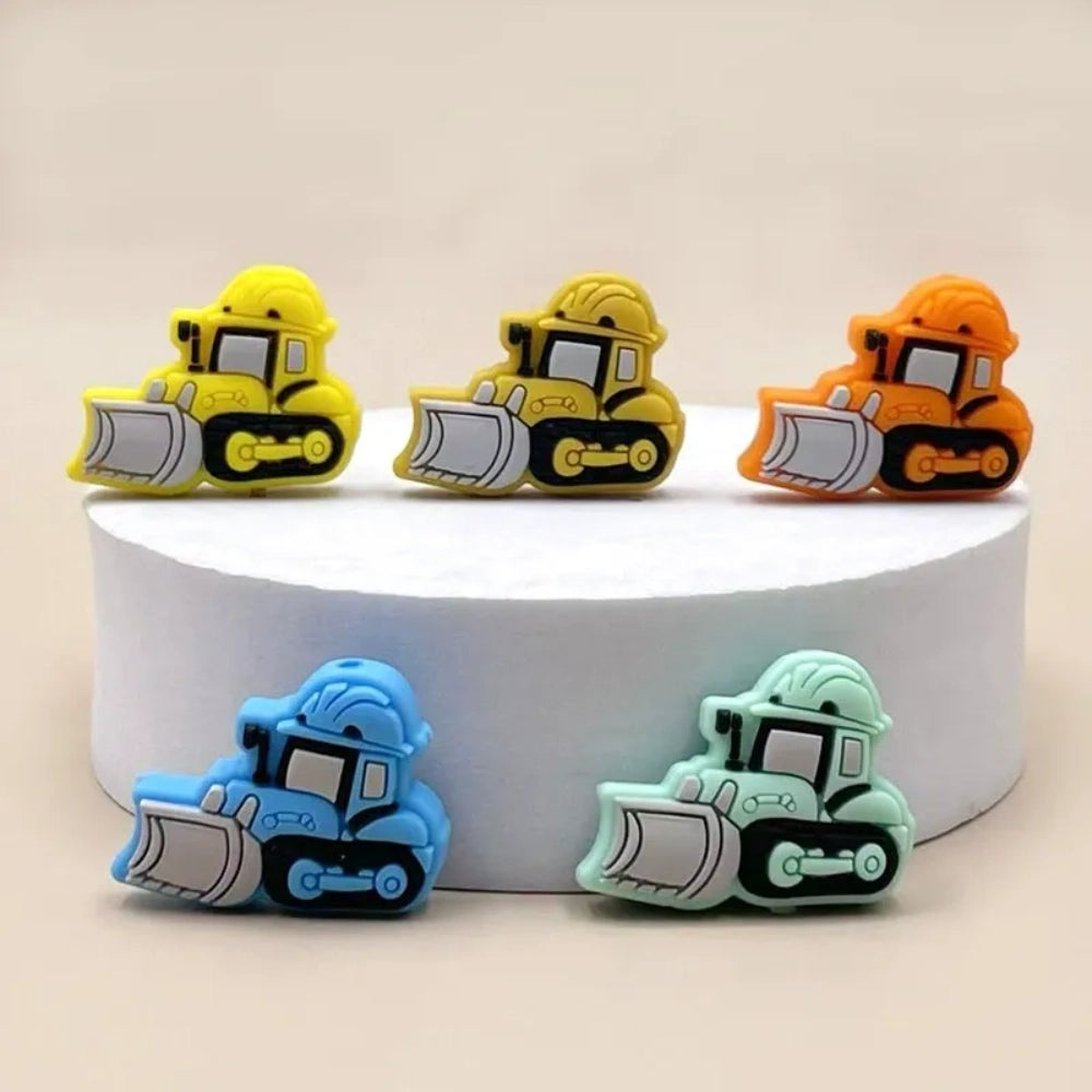 Five colorful silicone bulldozer construction truck focal beads in yellow, dark yellow, orange, blue, and mint green displayed on a white round platform - Random Mixed