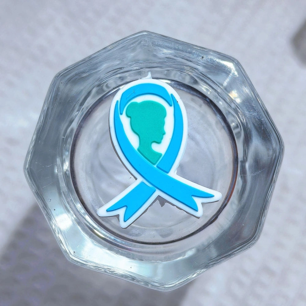Silicone 3D focal beads in cancer awareness designs including pink and blue awareness ribbons, decorative bows, and 'Her Fight Is My Fight' charms displayed alongside completed beadable pens on a white textured background. - 1