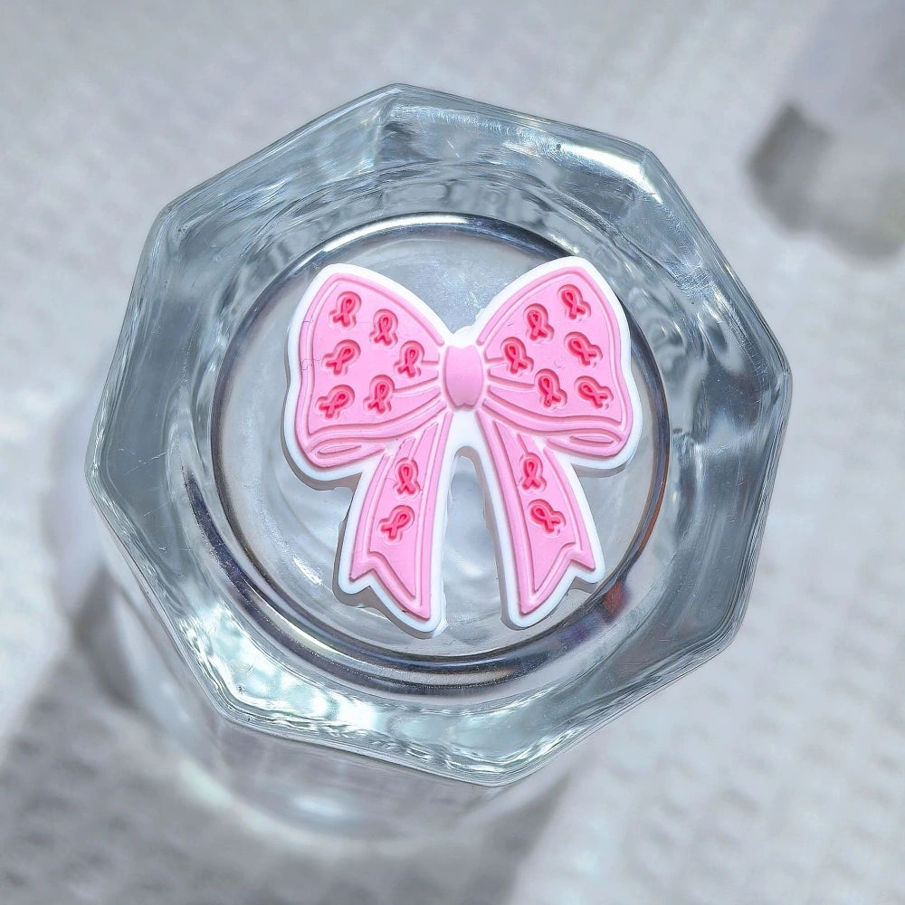 Silicone 3D focal beads in cancer awareness designs including pink and blue awareness ribbons, decorative bows, and 'Her Fight Is My Fight' charms displayed alongside completed beadable pens on a white textured background. - 2