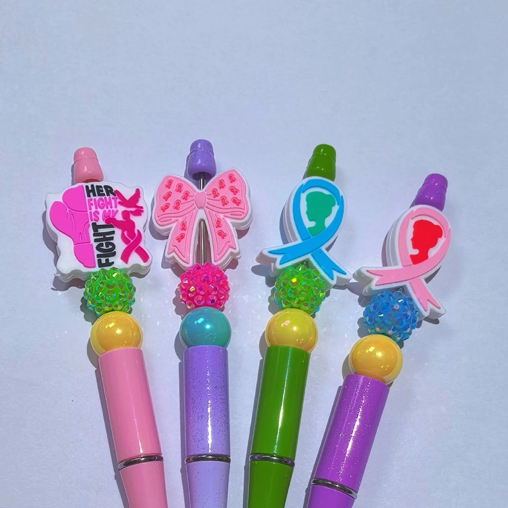 Silicone 3D focal beads in cancer awareness designs including pink and blue awareness ribbons, decorative bows, and 'Her Fight Is My Fight' charms displayed alongside completed beadable pens on a white textured background. - Random Mixed