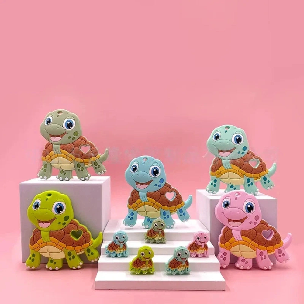 Cartoon turtle silicone focal beads in green, blue, yellow, and pink colors displayed on white pedestals against a pink background, available in large and small sizes for DIY crafts.