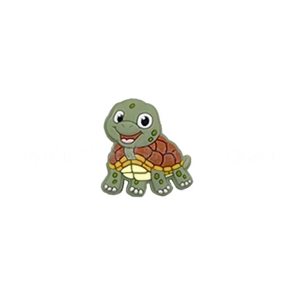 Cartoon turtle silicone focal beads in green, blue, yellow, and pink colors displayed on white pedestals against a pink background, available in large and small sizes for DIY crafts. - Matcha Green