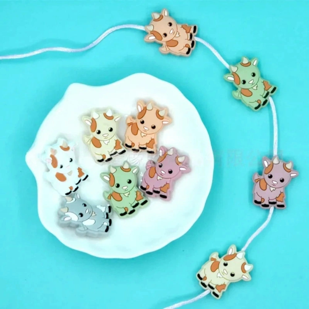 Assorted pastel color cute cow silicone focal beads displayed on a white shell dish and strung on a white cord against a teal background, available in gray, green, pink, tan, and white colorways. - Random Mixed