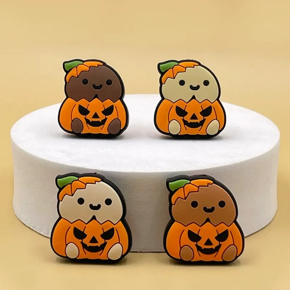 Four cute silicone focal beads featuring cartoon critters sitting inside jack-o-lantern pumpkin costumes, available in light and brown character skin tones, displayed on a white platform with a warm beige background.