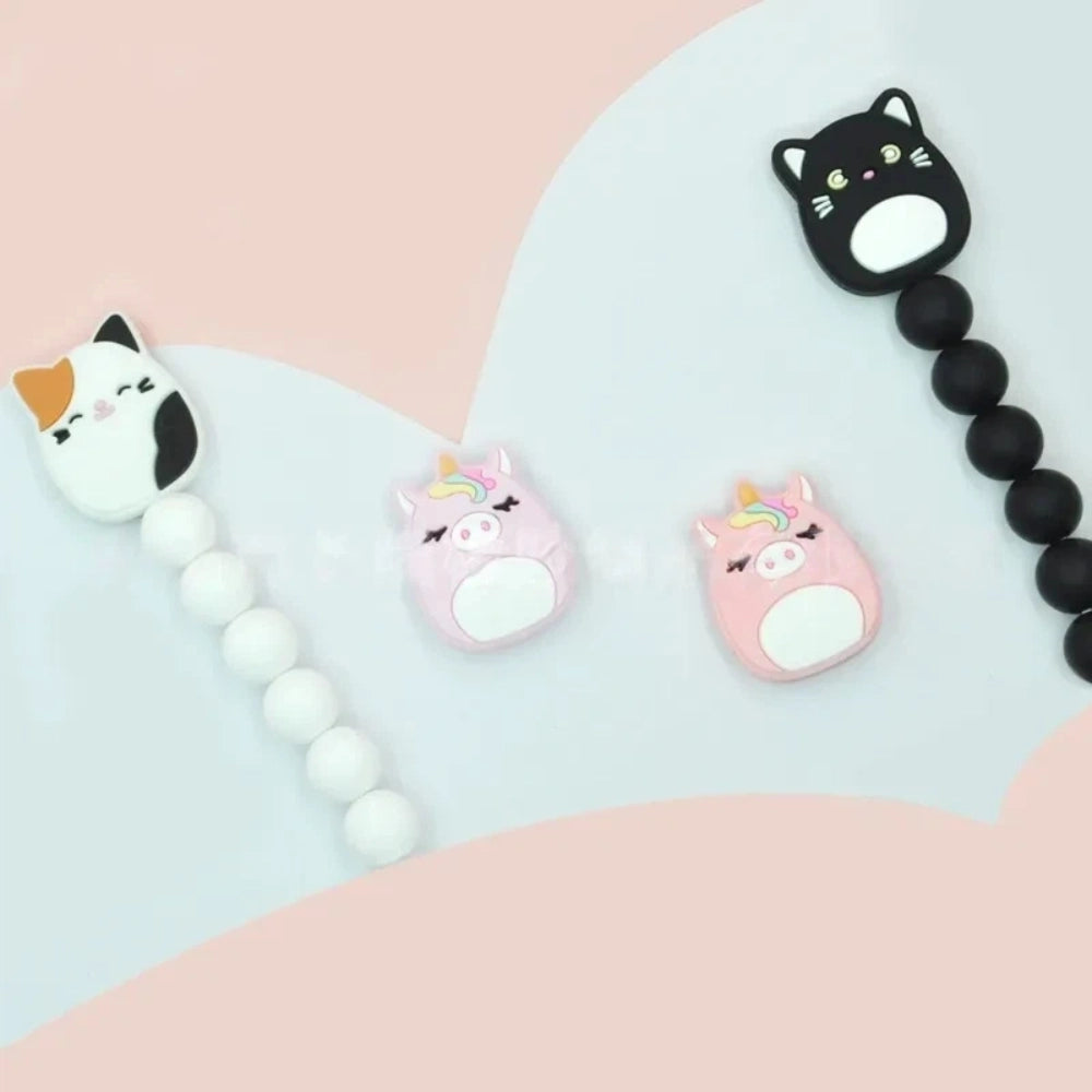 Kawaii silicone focal beads featuring black cat, calico cat, and pink unicorn characters on beaded strands in black and white, displayed on a pastel background for DIY craft projects.