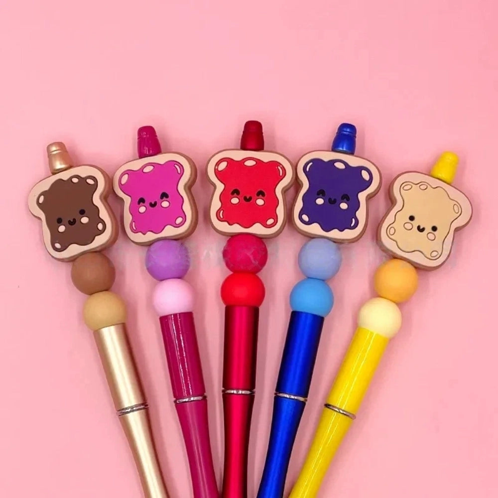 Five kawaii toast spread silicone focal beads in chocolate, pink jam, red jam, grape jam, and peanut butter designs, displayed on colorful beadable pens against a pink background.