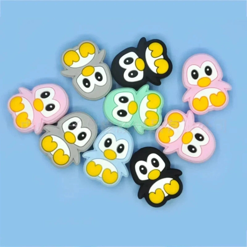 Assorted color cute cartoon penguin silicone focal beads in black, pink, gray, blue, and mint green on a light blue background, perfect for beadable pens, keychains, and badge reels.