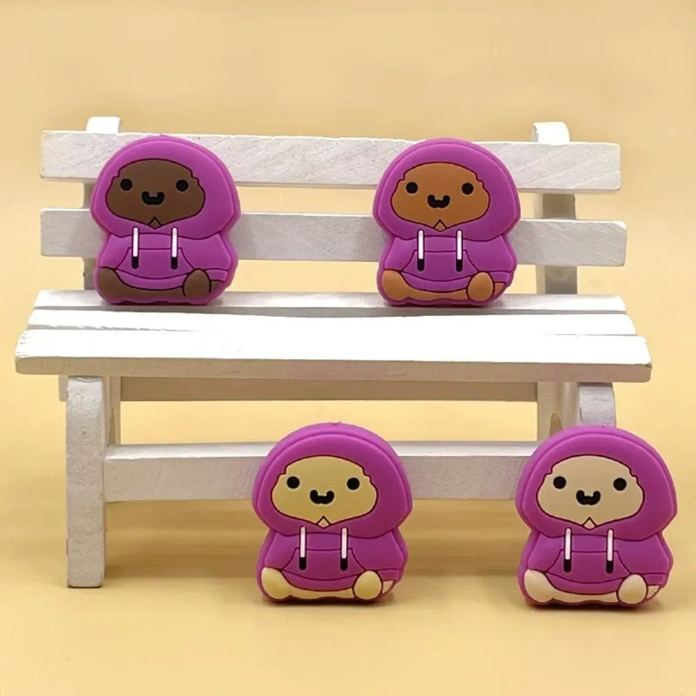 Four purple hoodie bear silicone focal beads in varying skin tones, sitting pose, displayed on a miniature white wooden bench with yellow background.