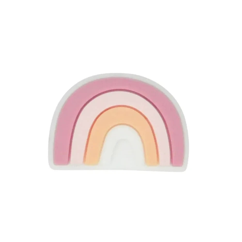 Five colorful silicone rainbow arch focal beads in various color combinations including blue-gray, multicolor, dark-mint, boho pink, and pink-teal, displayed on a wooden slice with pine cones on a star-patterned surface. - Pink