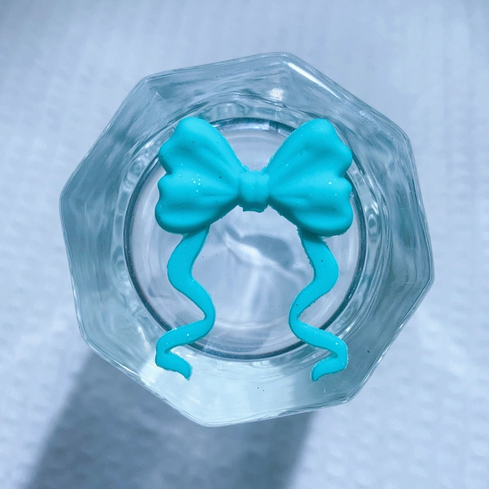 8 assorted ribbon bow silicone focal beads in purple, mint, teal swirl, hot pink, white, black glitter, turquoise, and light pink, displayed on white waffle fabric background. - 5