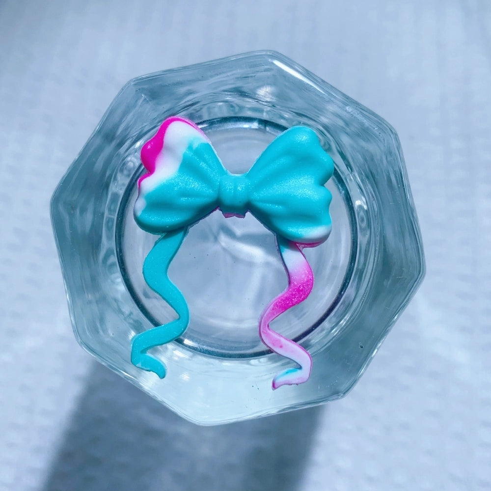 8 assorted ribbon bow silicone focal beads in purple, mint, teal swirl, hot pink, white, black glitter, turquoise, and light pink, displayed on white waffle fabric background. - 7