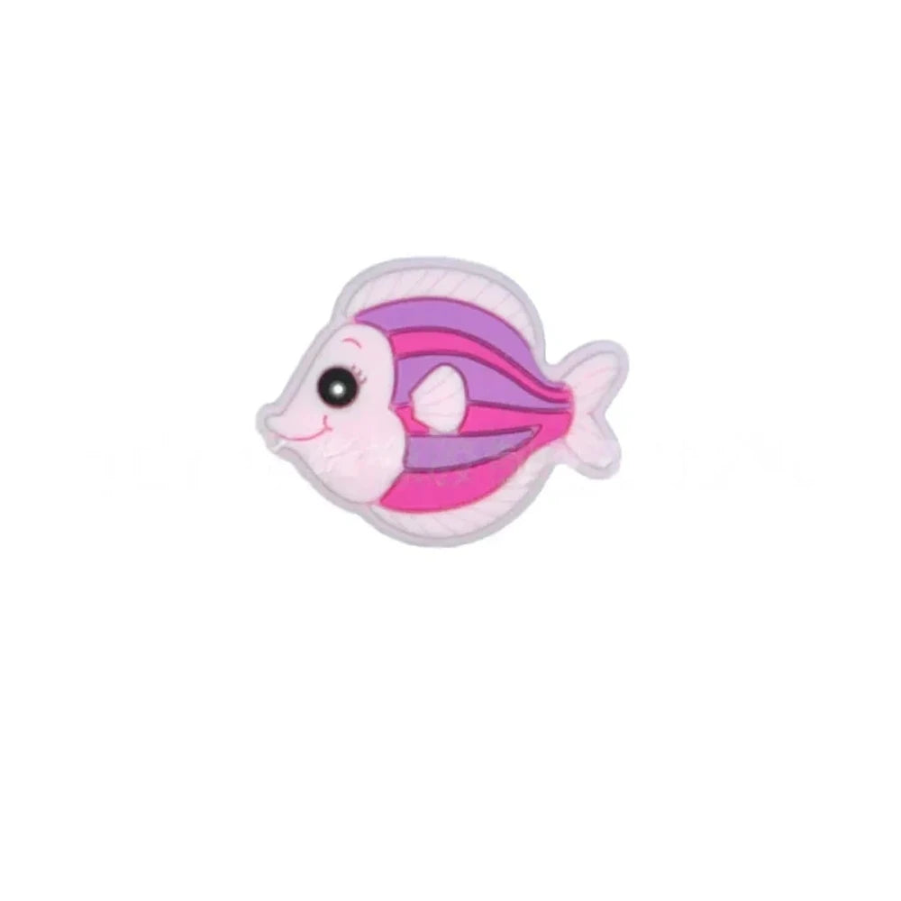 Five colorful cartoon tropical fish silicone focal beads in teal, olive green, blue, pink, and gray displayed on a miniature white wooden bench against a blue background. - Light Pink