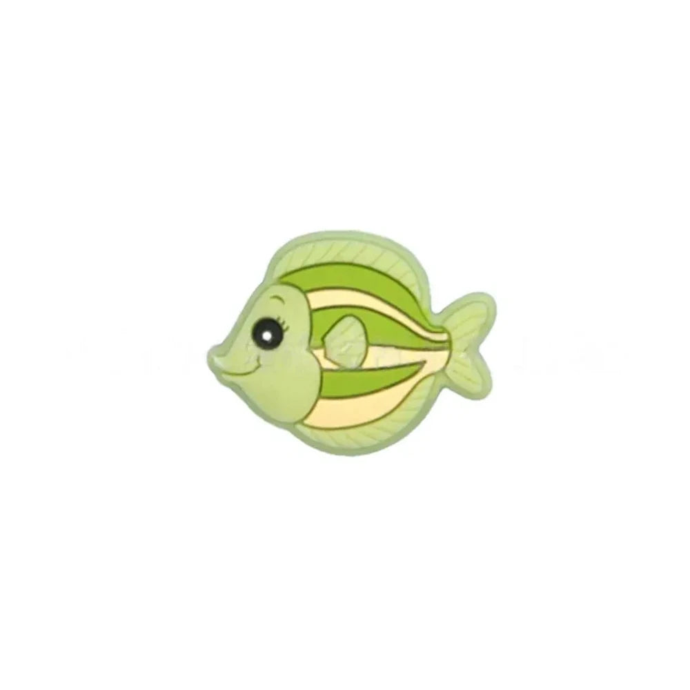Five colorful cartoon tropical fish silicone focal beads in teal, olive green, blue, pink, and gray displayed on a miniature white wooden bench against a blue background. - Matcha Green