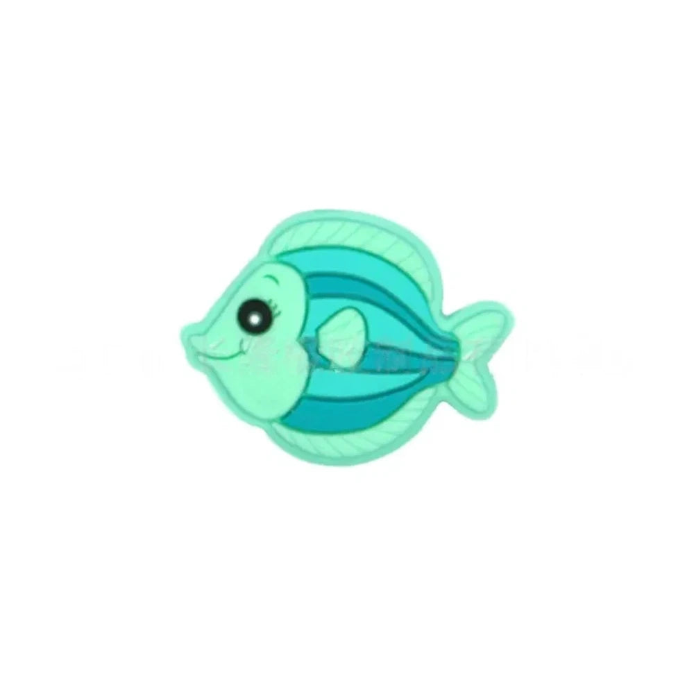 Five colorful cartoon tropical fish silicone focal beads in teal, olive green, blue, pink, and gray displayed on a miniature white wooden bench against a blue background. - Mint Green