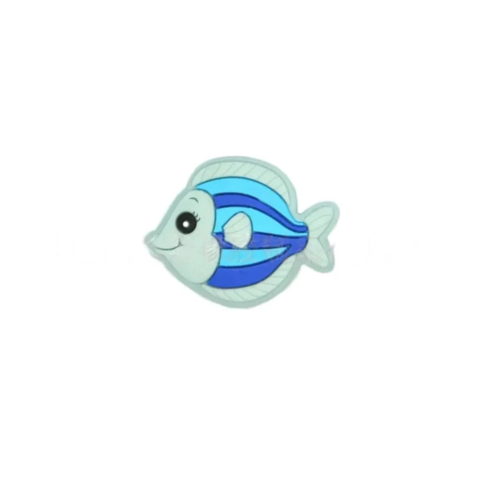 Five colorful cartoon tropical fish silicone focal beads in teal, olive green, blue, pink, and gray displayed on a miniature white wooden bench against a blue background. - Royal Blue