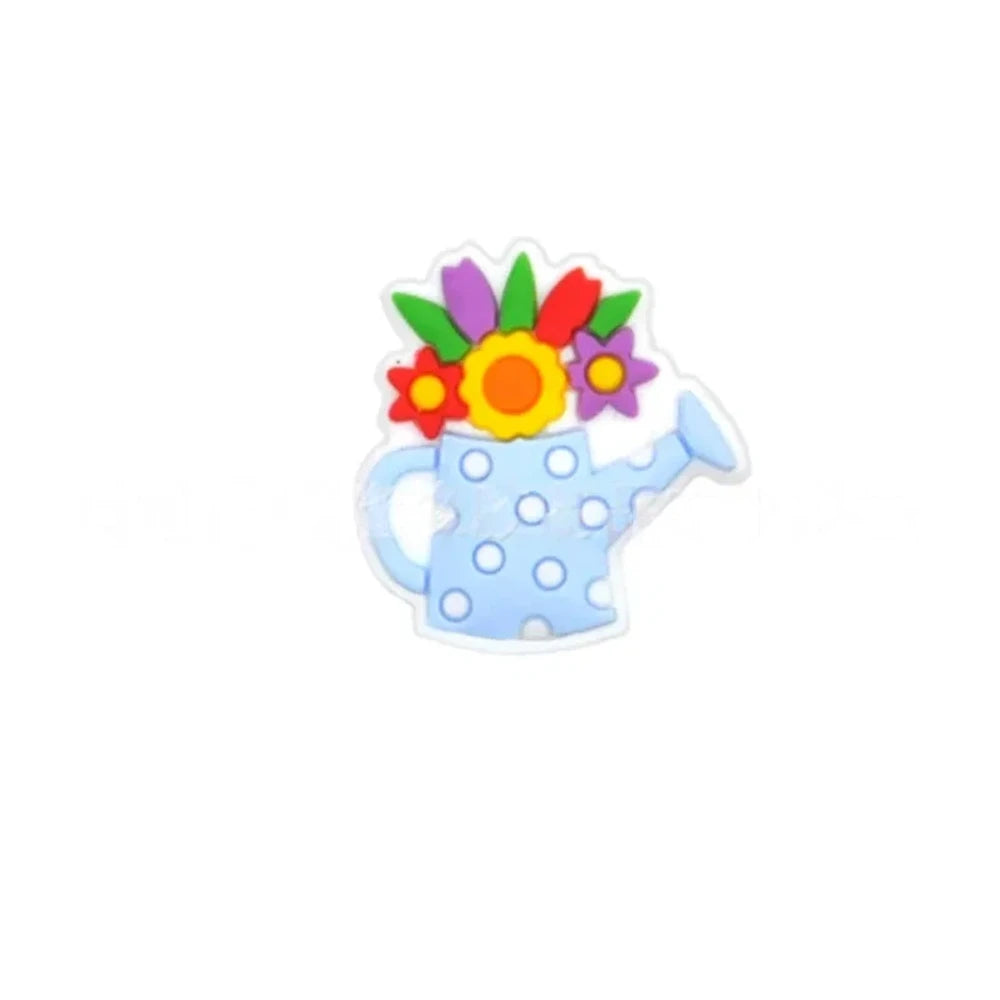 Five colorful silicone focal beads shaped like polka dot watering cans with 3D flower bouquets on top, displayed in pink, peach, blue, teal, white, and black colorways on a pink surface with a white picket fence backdrop. - Light Blue