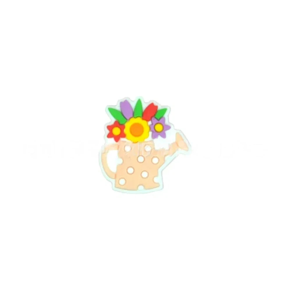 Five colorful silicone focal beads shaped like polka dot watering cans with 3D flower bouquets on top, displayed in pink, peach, blue, teal, white, and black colorways on a pink surface with a white picket fence backdrop. - Orange