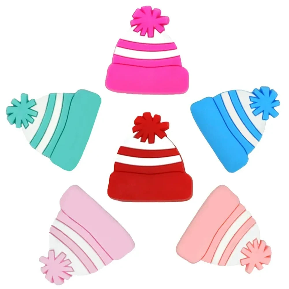 Six colorful silicone winter beanie hat focal beads with pom poms in hot pink, teal, blue, red, light pink, and peach arranged in a star pattern on a white background.